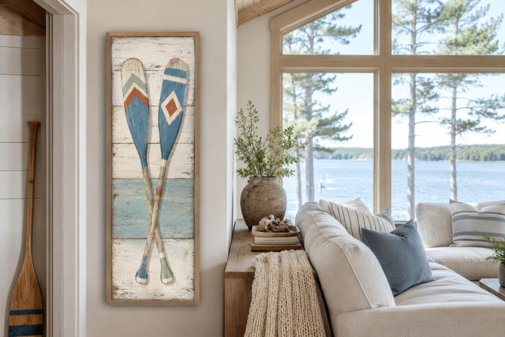 Tall narrow canvas wall art featuring two crossed rustic oars in blue and cream on a wood backdrop.