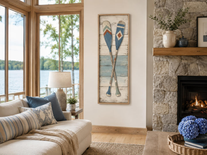 Tall narrow canvas wall art featuring two crossed weathered oars in blue and cream on a white wall.