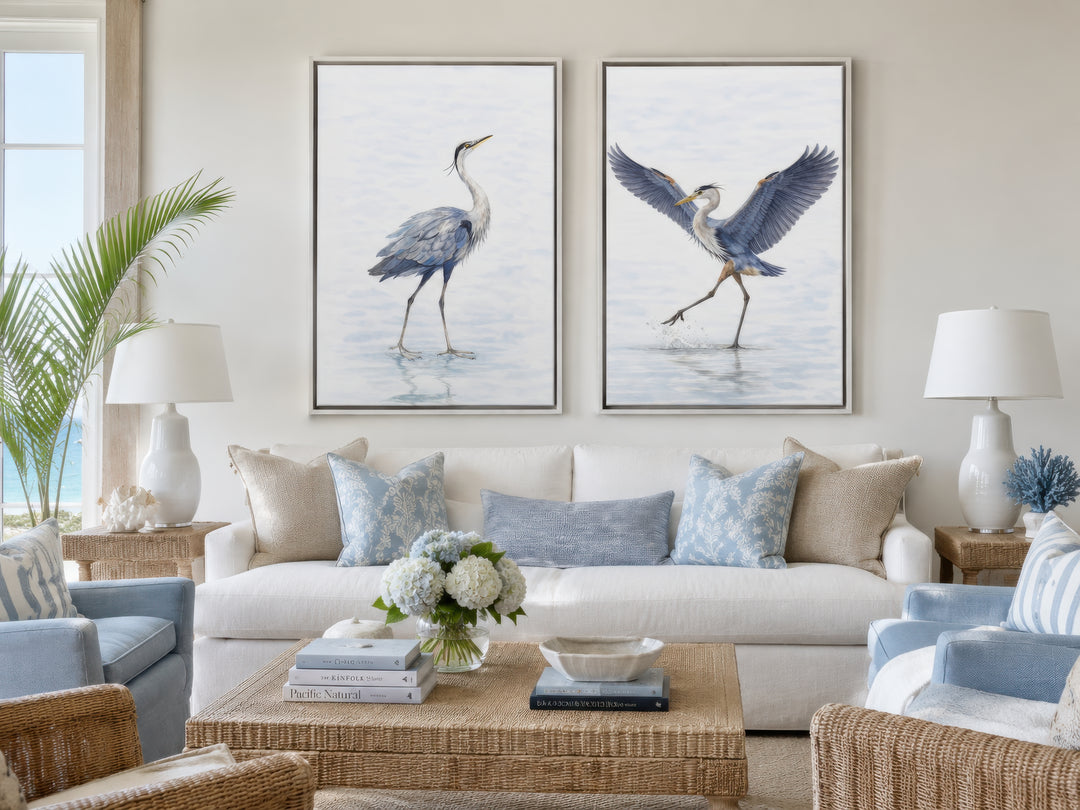 Set of two watercolor heron bird canvas prints in a coastal living room above a white sofa.