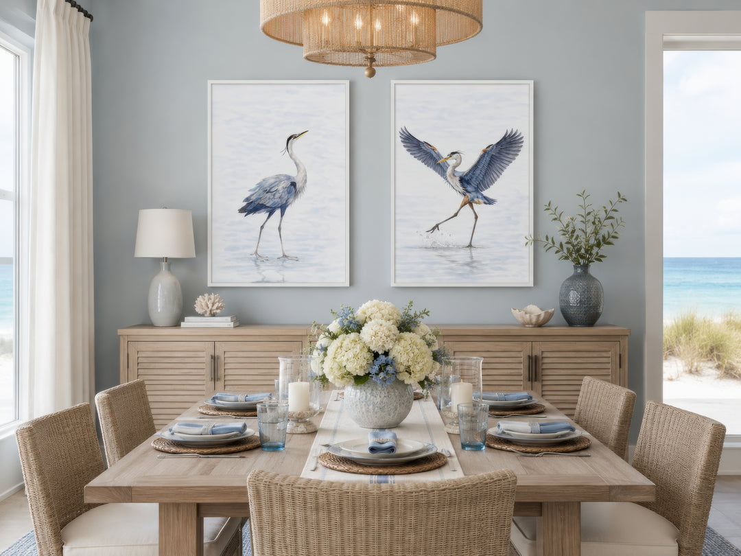 Set of two watercolor heron bird canvas prints in white frames above a wooden sideboard.