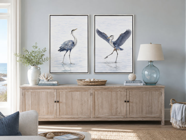 Set of two watercolor heron canvas prints in white frames above a light wood sideboard.