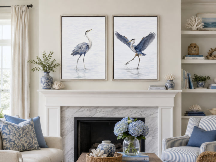 Set of two watercolor heron canvas prints in silver frames hanging above a white fireplace mantel.