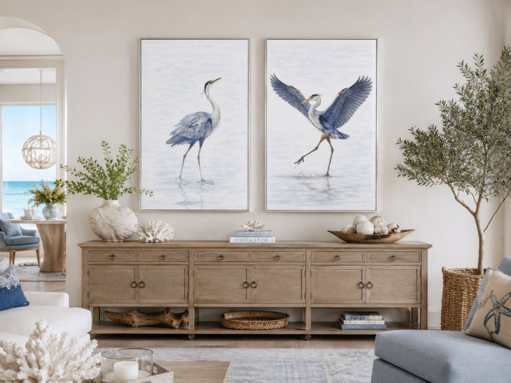 Set of two watercolor heron bird canvas prints in silver frames above a wooden console table.