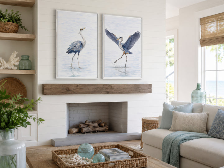 Set of two watercolor heron bird canvas prints hanging above a fireplace in a coastal living room.