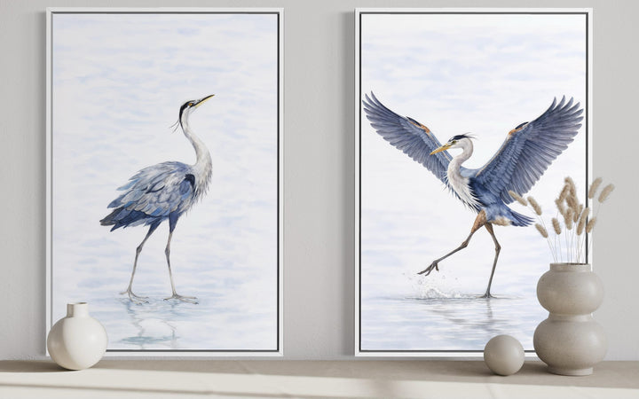 Set of two watercolor heron canvas prints in white frames, styled with neutral vases on a shelf.