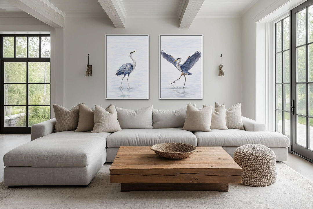 Two watercolor canvas prints of dancing herons in a neutral, modern living room setting.