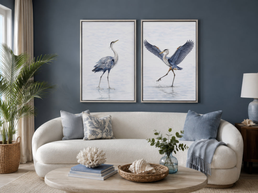 Set of two watercolor heron bird canvas prints in silver frames above a white sofa in a living room.