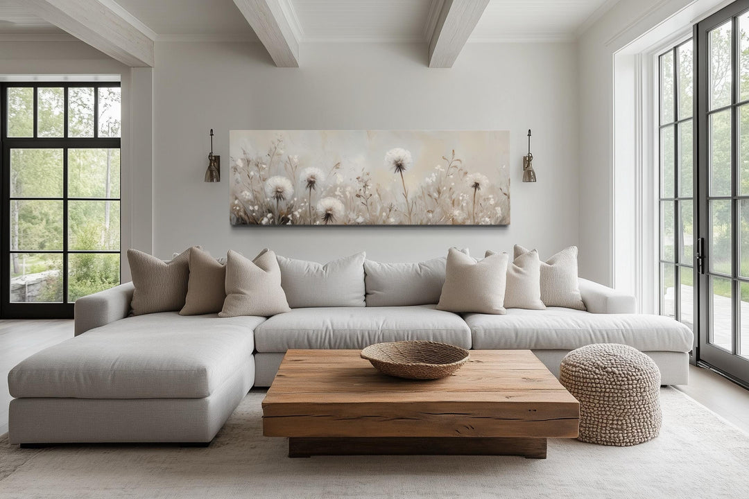 Long horizontal wall art of white dandelions in a neutral farmhouse living room above a sofa.
