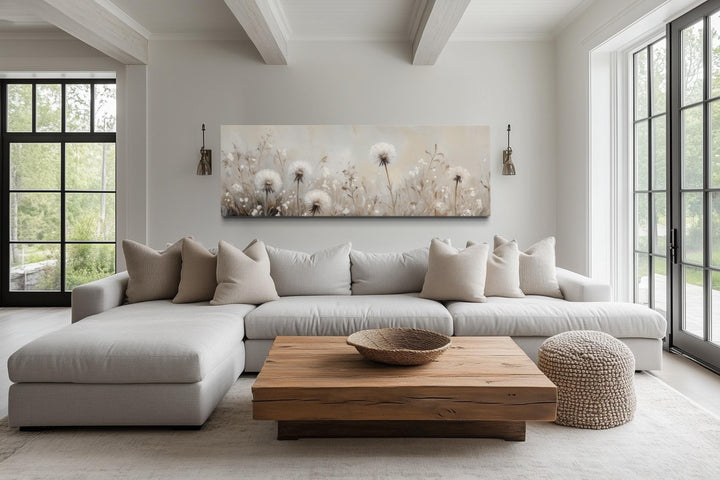 Long horizontal wall art of white dandelions in a neutral farmhouse living room above a sofa.