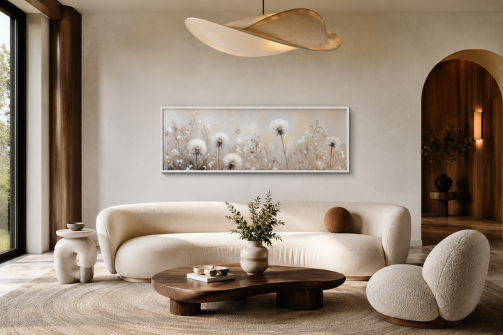 Long horizontal wall art of white dandelions in neutral beige tones above a modern curved sofa.