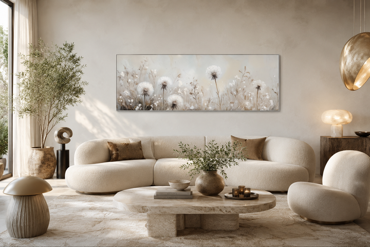 Long horizontal wall art of white dandelions in neutral beige tones above a modern curved sofa.