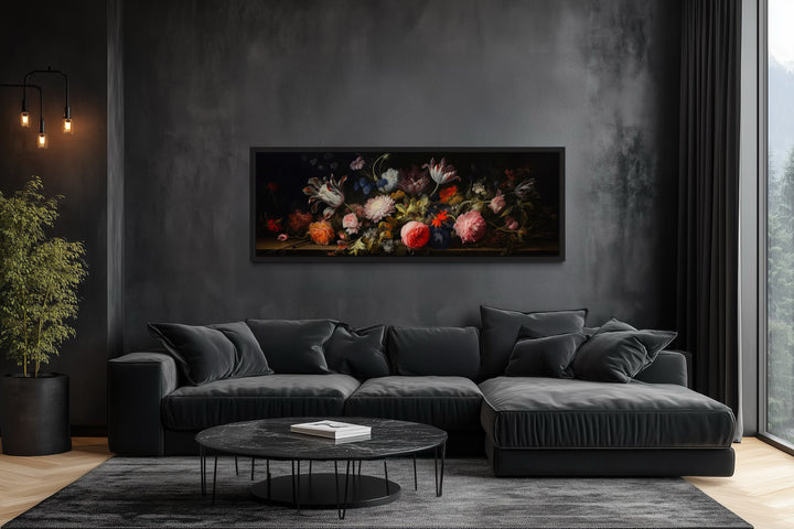 Horizontal framed canvas wall art of moody antique flowers above a black sofa in a dark room.