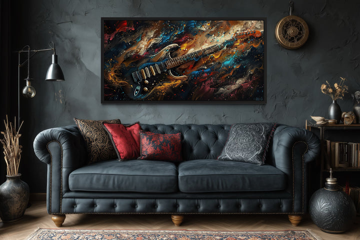Framed canvas wall art of a dark, colorful abstract electric guitar above a black leather sofa.