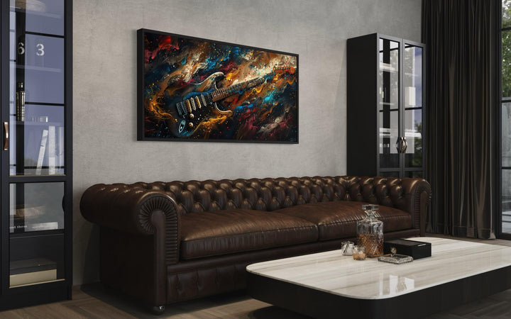 Dark colorful electric guitar framed canvas wall art above a brown leather sofa in a music room.