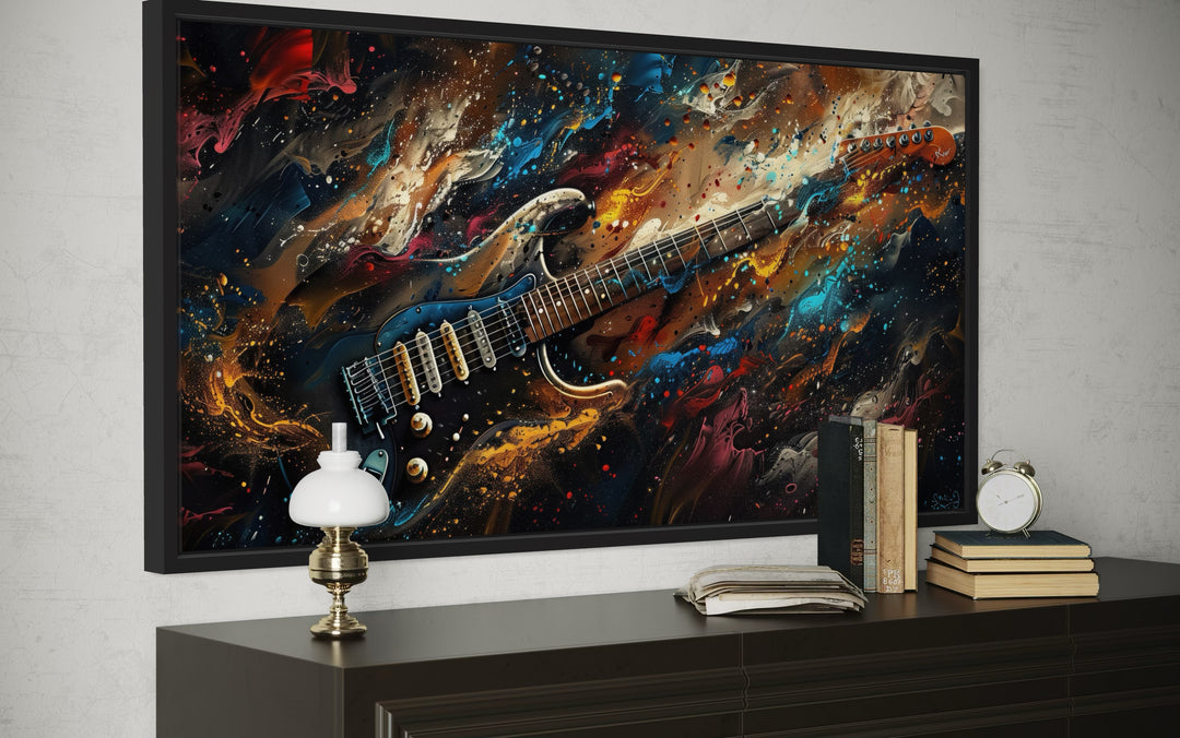 Dark colorful electric guitar framed canvas wall art above a dark wood dresser with books and lamp.