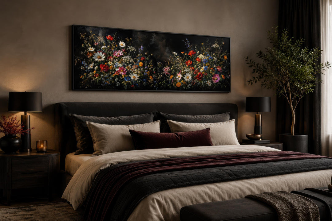 Long narrow canvas print of colorful wildflowers on a dark background above a bed in a moody room.
