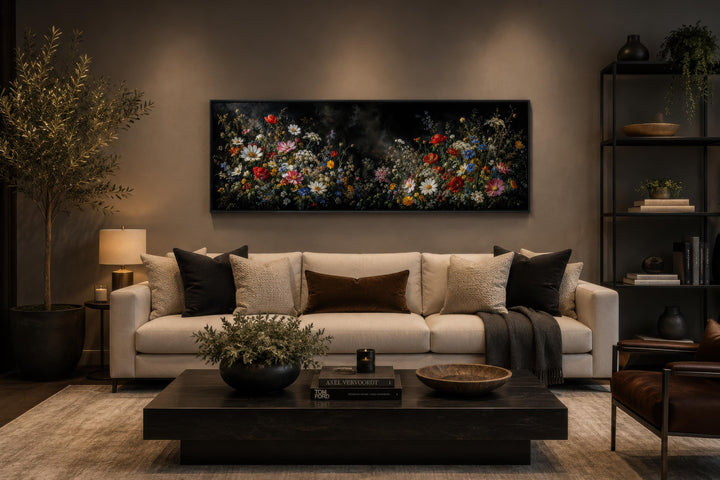 Long narrow canvas print of dark moody wildflowers above a sofa in a modern living room.