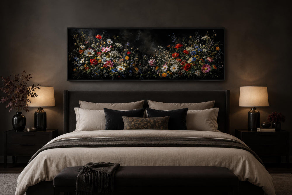 Long narrow canvas print of colorful wildflowers on a dark background above a bed in a moody room.