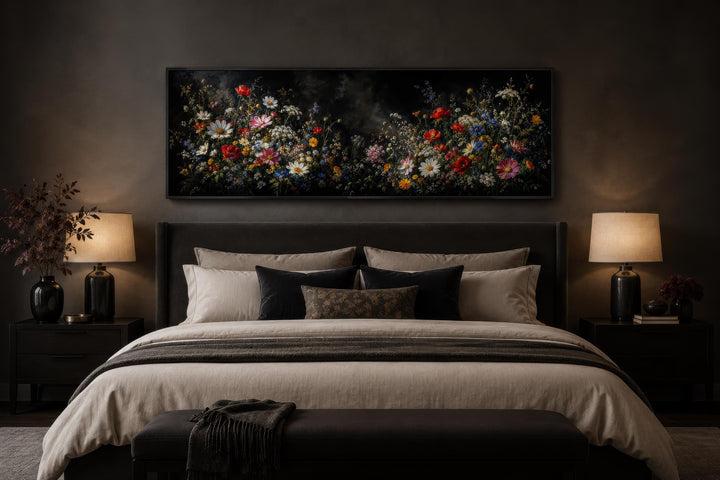 Long narrow canvas print of colorful wildflowers on a dark background above a bed in a moody room.