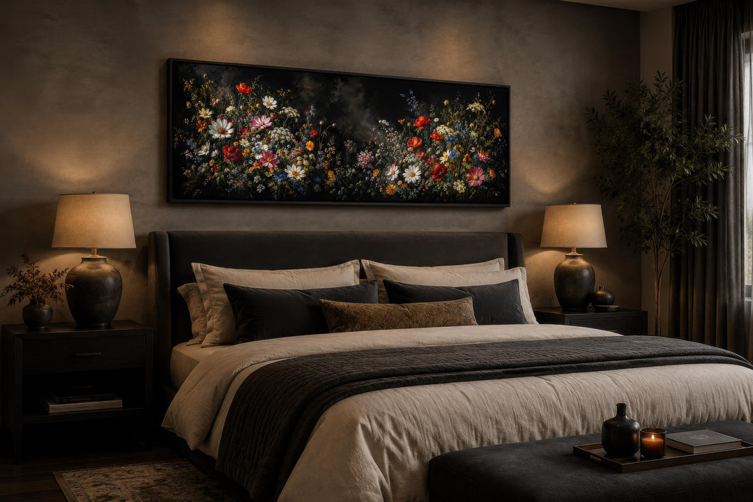 Long narrow canvas print of colorful wildflowers on a dark background above a bed in a moody room.