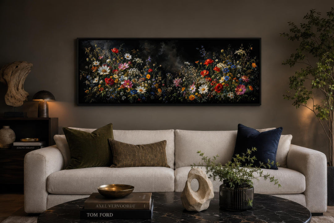 Long narrow canvas print of colorful wildflowers against a dark background above a modern sofa.