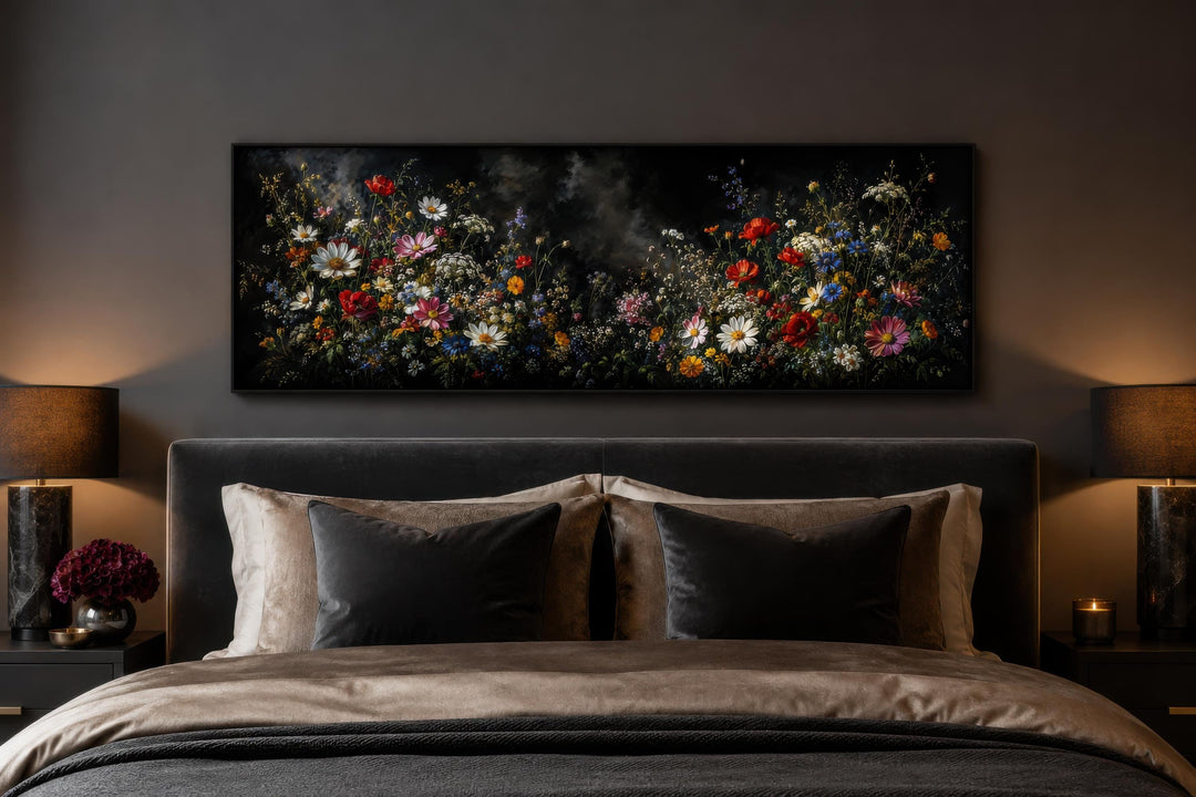 Long narrow canvas print of colorful wildflowers on a dark background above a bed in a moody room.