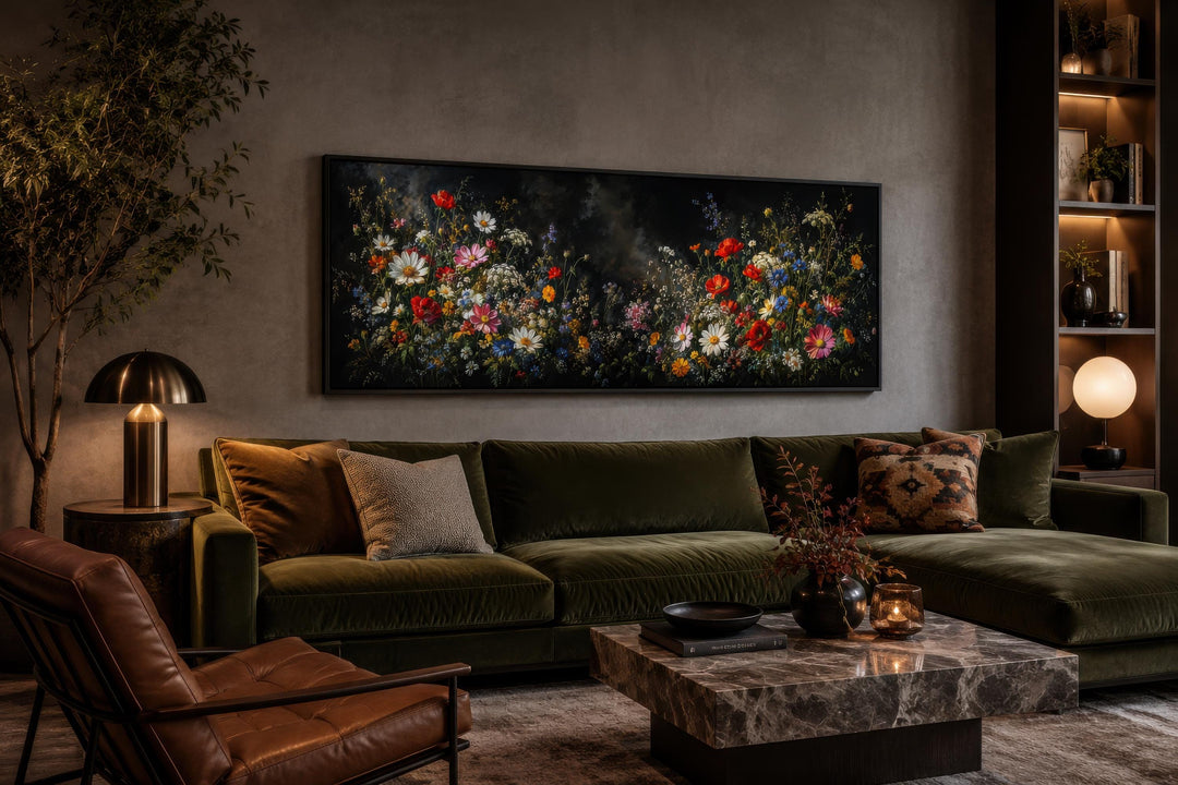 Long narrow canvas print of colorful wildflowers on a dark background above a green velvet sofa.