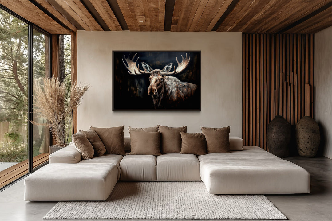 Dark moose painting framed canvas wall art hanging above a modern sofa in a rustic cabin living room
