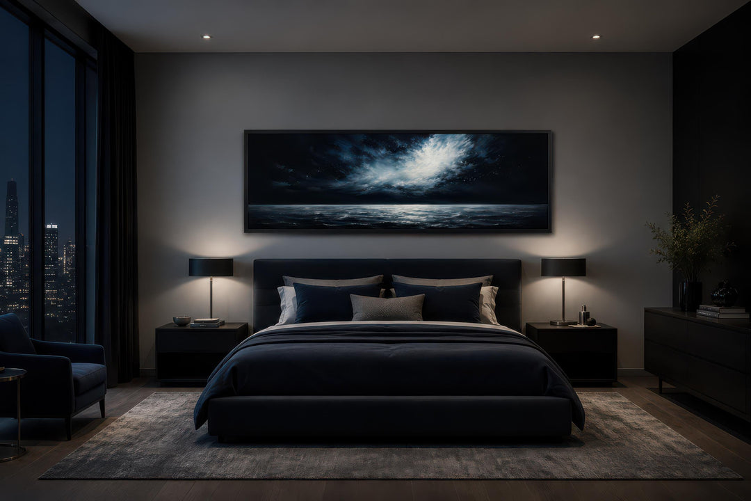 Dark navy moonlit ocean seascape canvas print hanging above a bed in a moody modern bedroom.