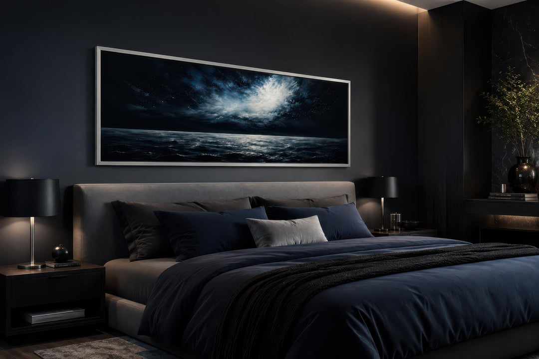 Wide horizontal canvas of a moonlit ocean storm hanging above a bed in a dark, modern bedroom.