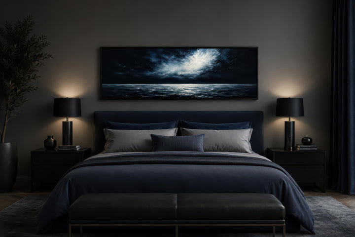Dark navy moonlit ocean seascape painting hanging above a bed in a moody, modern bedroom.