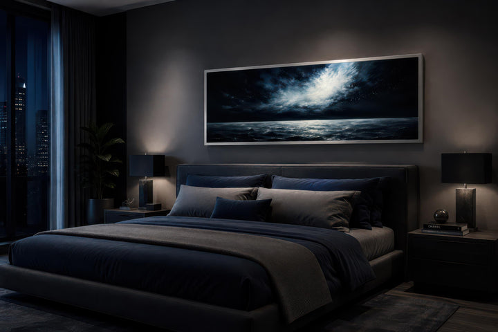 Wide horizontal seascape painting of a moonlit ocean at night above a bed in a dark bedroom.