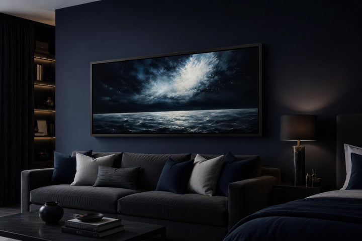 Dark navy moonlit ocean seascape painting hanging above a sofa in a moody, modern bedroom.