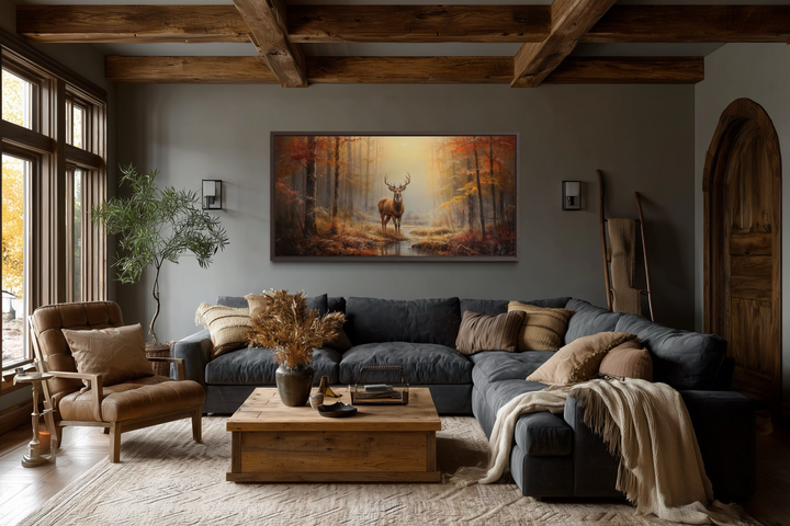 Large framed canvas print of a majestic stag in a golden autumn forest above a dark sectional sofa.