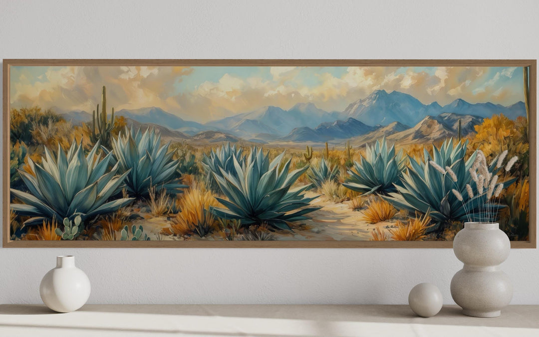 Panoramic desert agave painting in a wood frame above a console with minimalist vases.