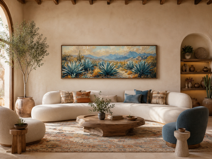 Panoramic desert agave painting in a wooden frame above a curved sofa in a southwestern living room.