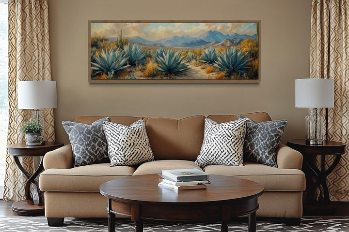 Panoramic desert agave painting in a wooden frame above a tan sofa with southwestern pillows.