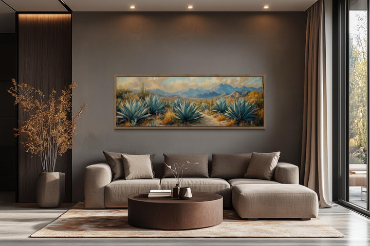 Panoramic desert agave painting in a wooden frame above a modern sofa in a neutral living room.