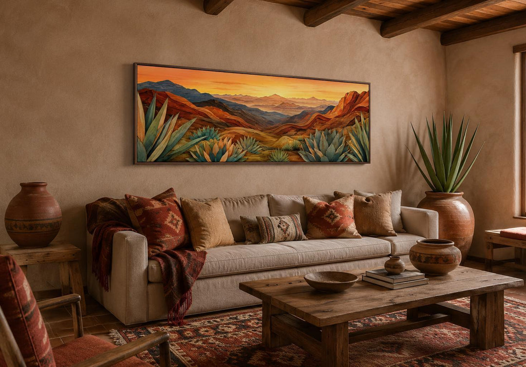 Wide horizontal canvas print of a desert agave landscape in terracotta and teal above a sofa.