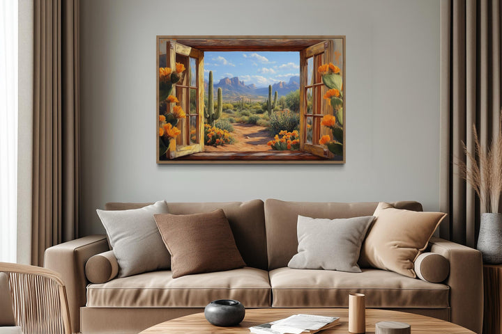 Desert cactus window view canvas wall art above a beige sofa in a modern living room.