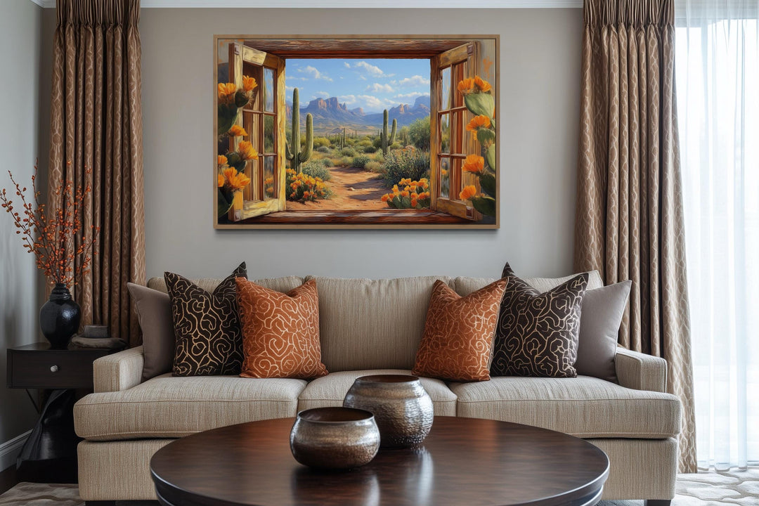 Desert cactus window view canvas wall art above a sofa with patterned pillows in a living room.