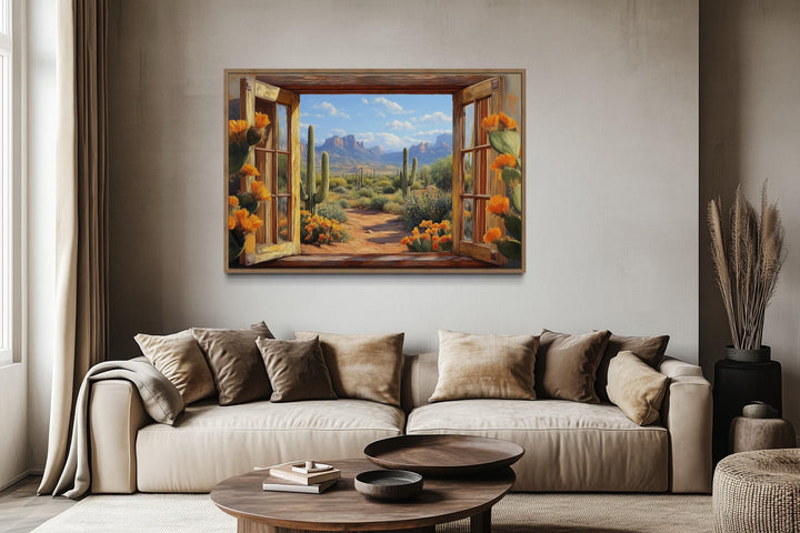 Desert cactus window view canvas wall art above a beige sofa in a modern living room.