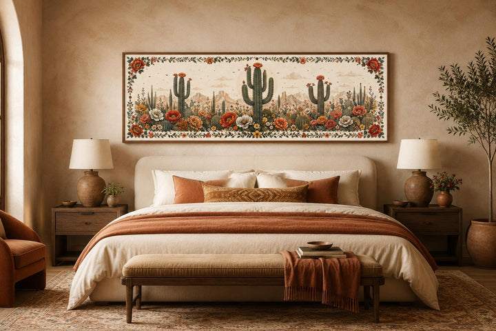 Long narrow canvas wall art of blooming saguaro cacti and desert flowers above a bed.