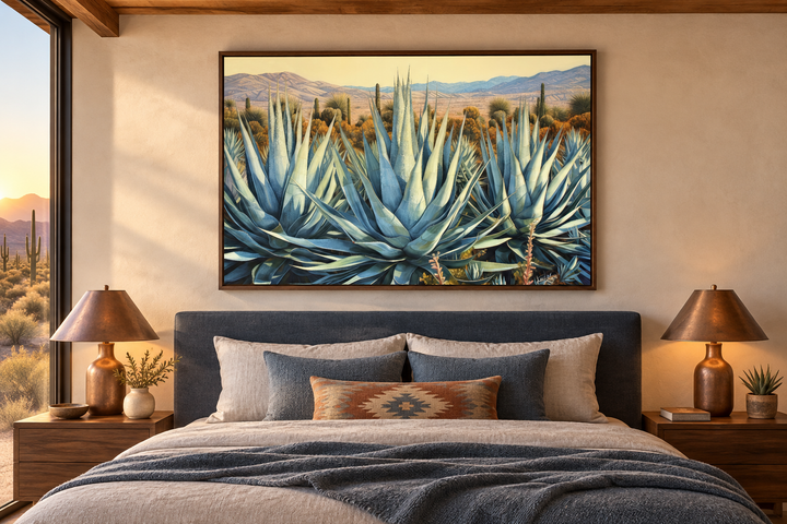 Framed canvas wall art of blue agave plants in a desert landscape above a bed in a modern bedroom.