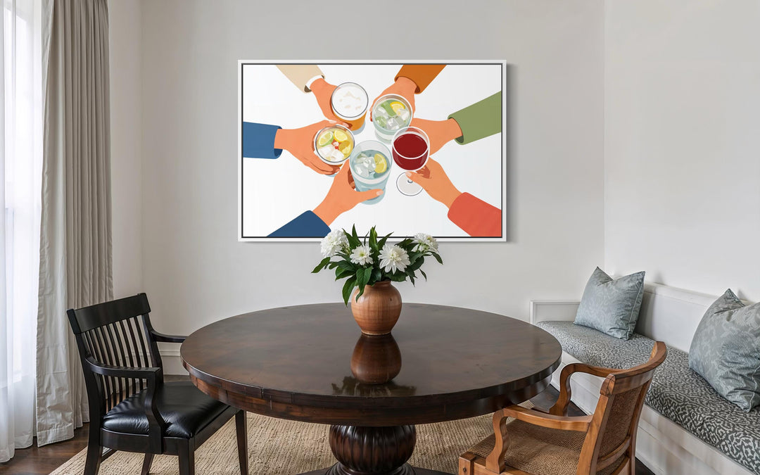 A modern canvas print of friends toasting drinks hangs above a round wooden dining table.