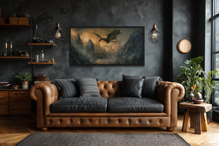 Framed panoramic canvas art of a dragon flying over misty mountains above a brown leather sofa.