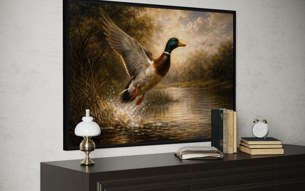 A framed canvas print of a mallard duck in flight over a river, displayed above a dark wood dresser.