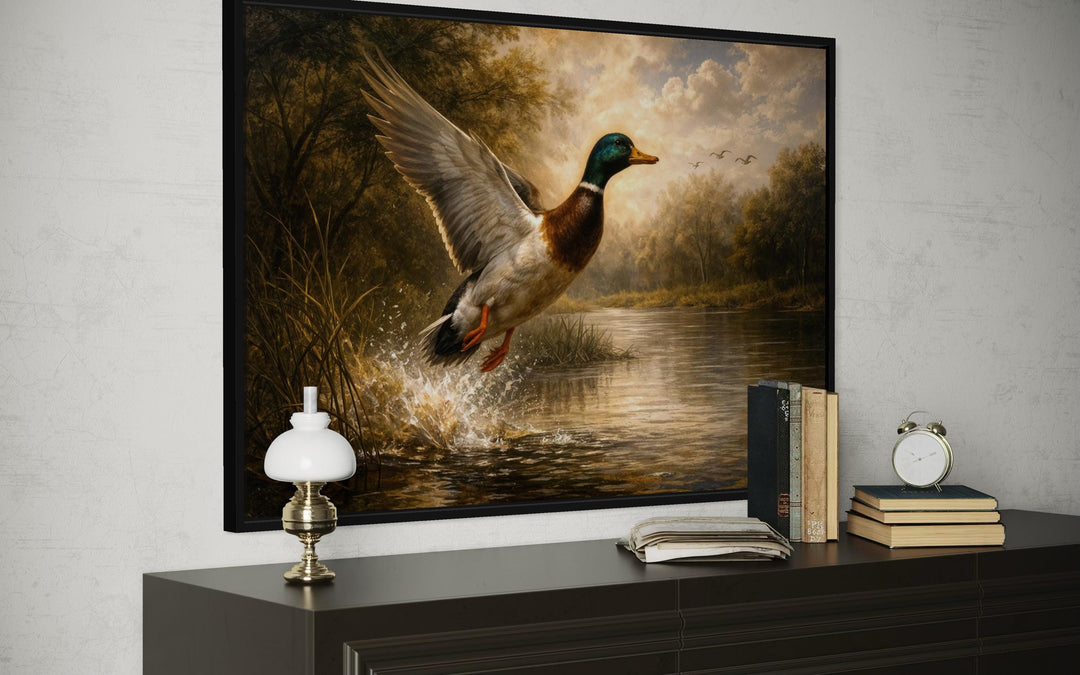 A framed canvas print of a mallard duck in flight over a river, displayed above a dark wood dresser.