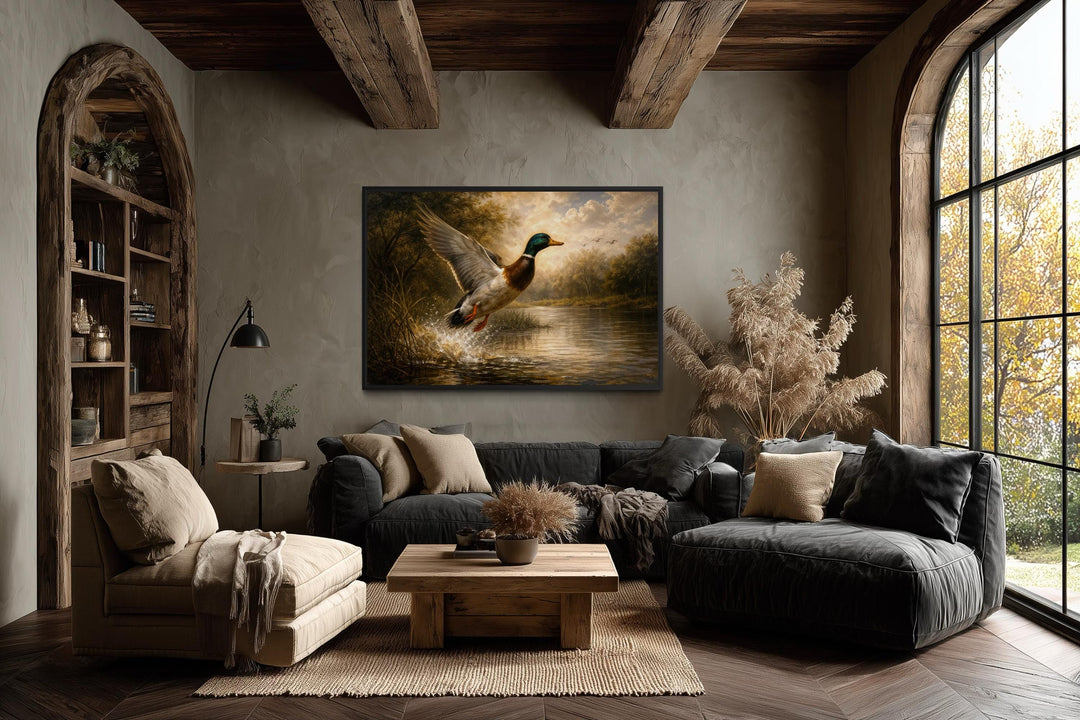A framed canvas print of a mallard duck in flight over a river hangs in a rustic, wood-beamed room.