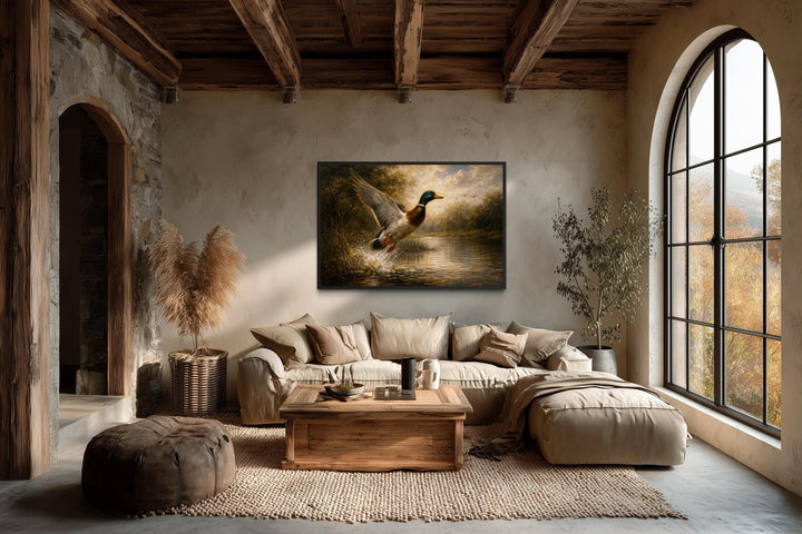 A framed canvas print of a mallard duck in flight over a river in a rustic, earth-toned living room.